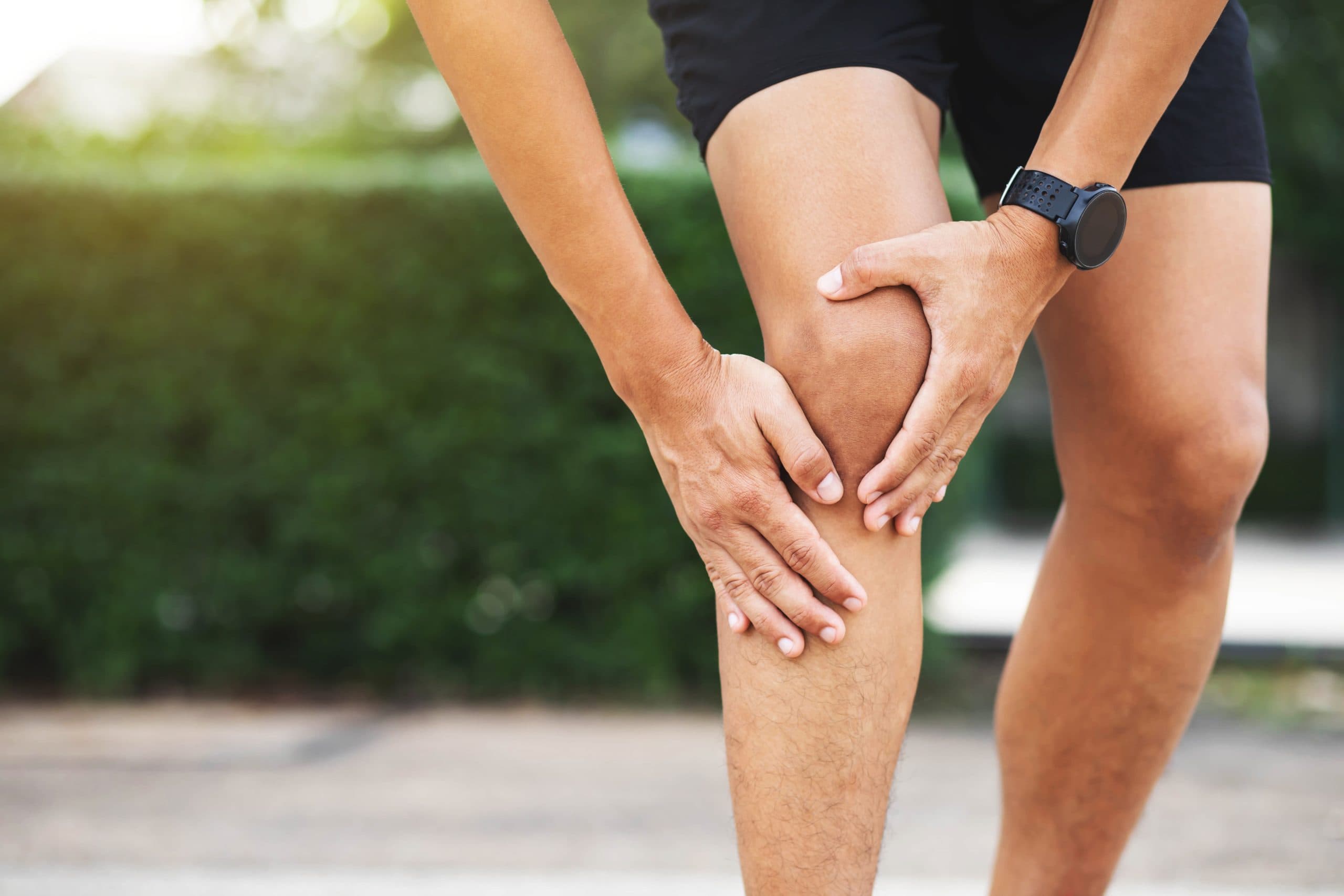 Runner holding knee outdoors due to pain